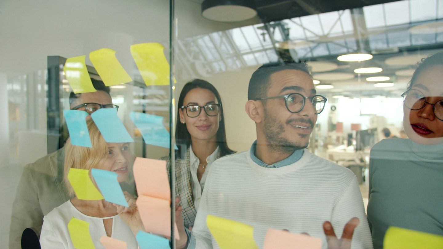 Diverse team brainstorming ideas with sticky notes on glass.